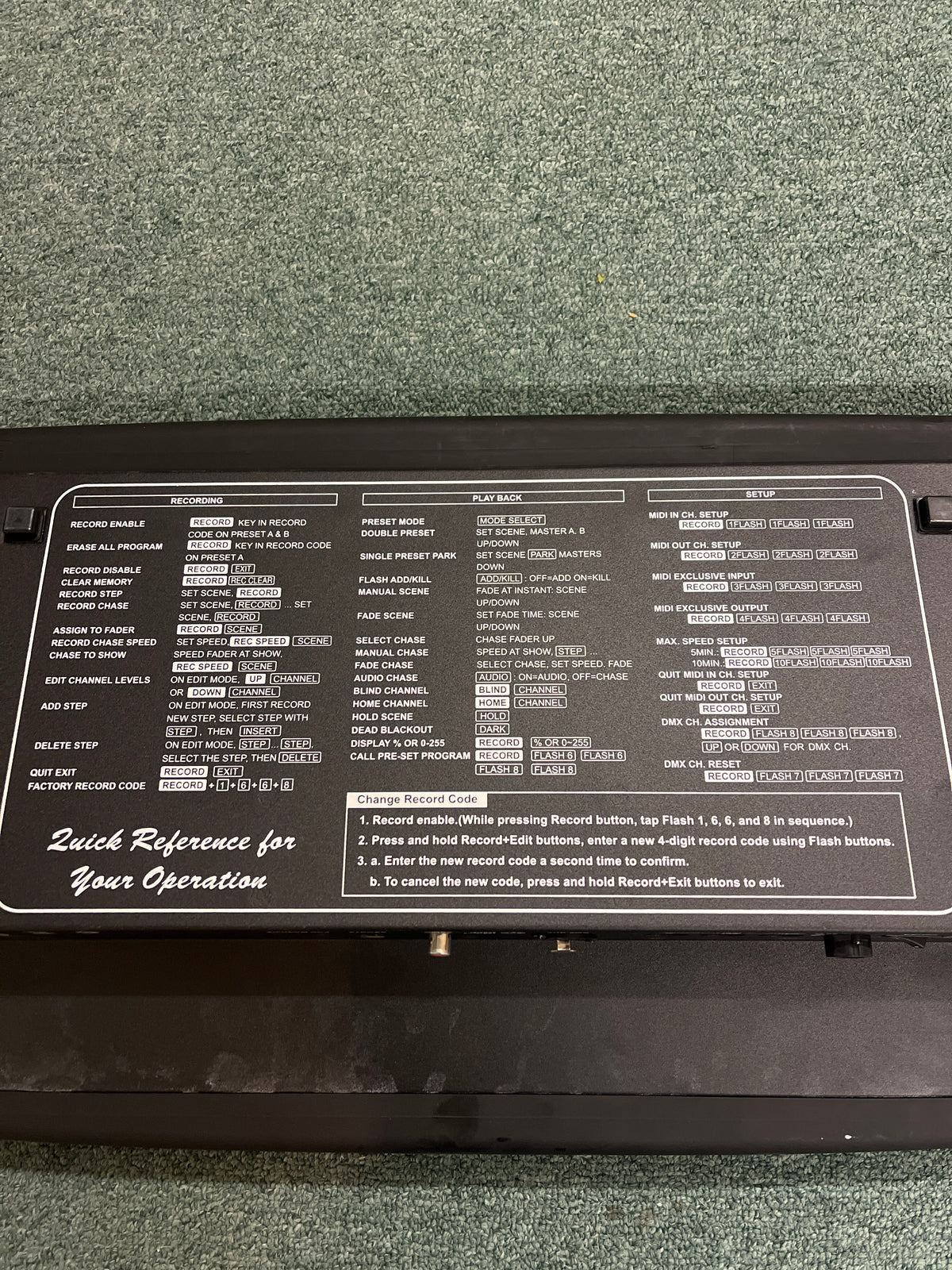 The Elation Scene Setter 24-Channel DMX Dimmer Console features a black control panel with white text and button labels, showing programming and playback instructions. It is placed on green carpet, providing efficient lighting control for any setup.
