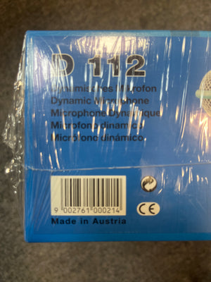 Close-up of a blue AKG D112 Dynamic Microphone NOS box, wrapped in clear plastic, showing multilingual text, barcode, and "Made in Austria" label. The AKG brand’s large-diaphragm mic is ideal for kick drums.