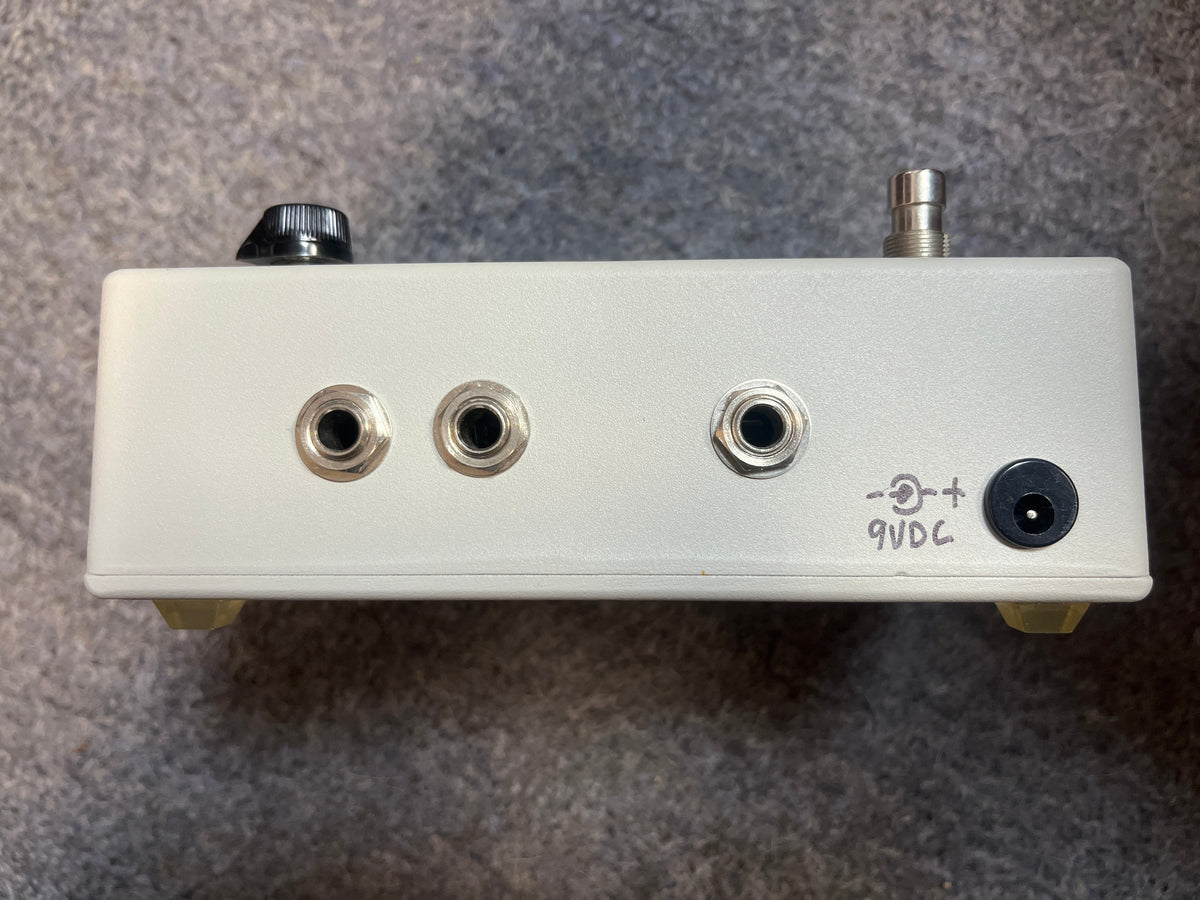 The preowned Switchazel Boutique AB/Y Switcher with Tuner Out by Switchazel features three audio jacks, a 9VDC input, a knob, and a footswitch—ideal for guitar amp switching or ground loop elimination. Shown on a gray surface.