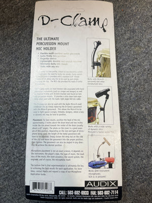Back of an Audix D-Clamp Percussion Mount Mic Holder package by Audix, showing features, mounting instructions, compatibility details, and contact info on a gray carpet background.