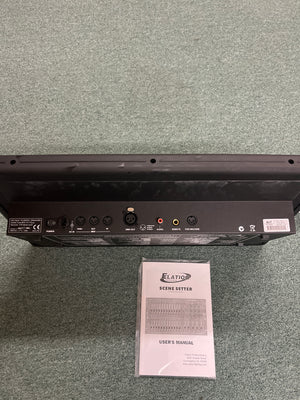 Back panel of the Elation Scene Setter 24-Channel DMX Dimmer Console by Elation, displaying multiple input/output ports, shown above its user manual on a carpeted floor—ideal for professional lighting control and scene programming.