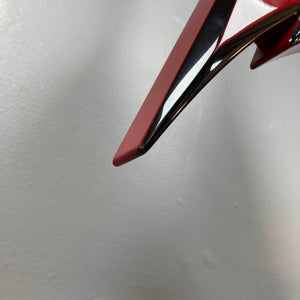 Close-up of a shiny red and black Jackson Phil Demmel Demmelition King V electric guitar with a pointed edge, set against a plain light gray background, showcasing its iconic Floyd Rose tremolo system.