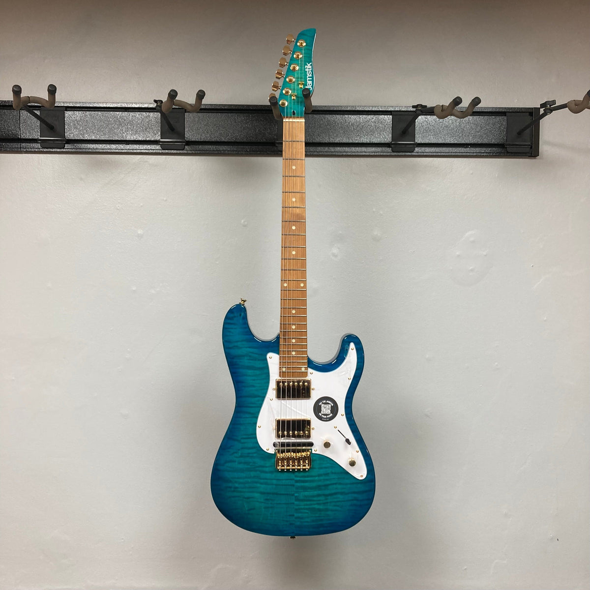 Jamstik Deluxe MIDI Blue Guitar w/Case on a wall hook, showcasing its electric design and industry-leading MIDI capabilities.