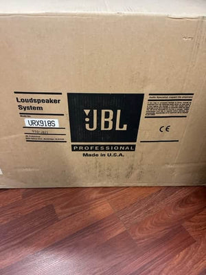 A cardboard box labeled "JBL Professional Loudspeaker System" sits on a wood floor, featuring the high-output VRX918S model for live sound reinforcement, with "Made in U.S.A." printed on the box.