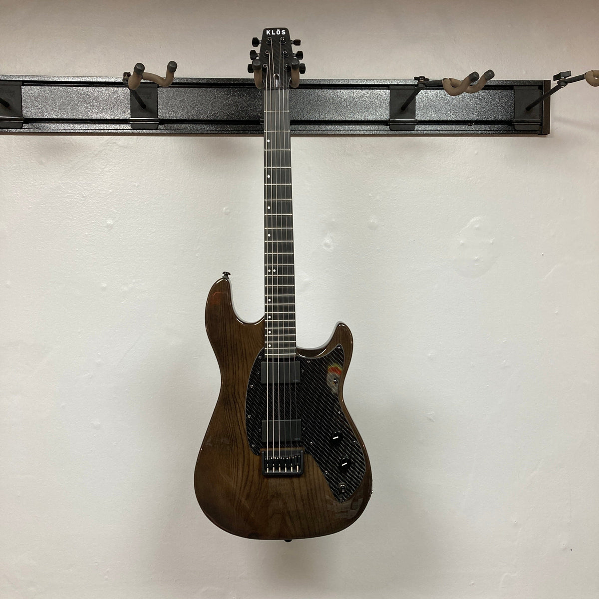 KLOS Apollo Pro Electric Guitar Dark Brown with a carbon fiber neck, displayed on a wall, showcasing its modern design and innovative features.