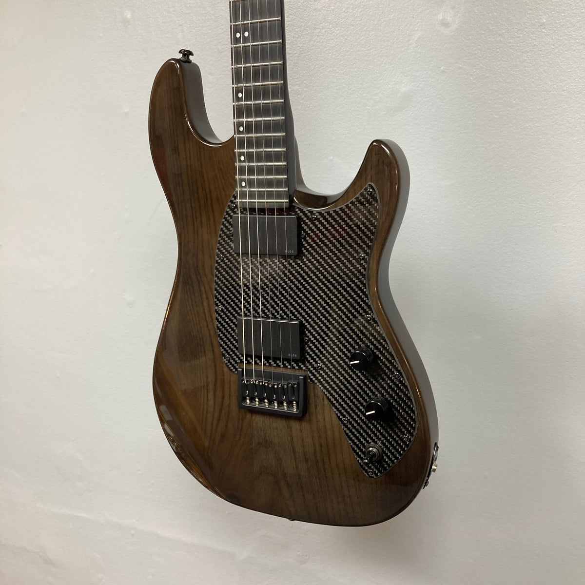 KLOS Apollo Pro Electric Guitar Dark Brown with an Ash body and carbon fiber neck, highlighted against a white wall, showcasing modern craftsmanship.