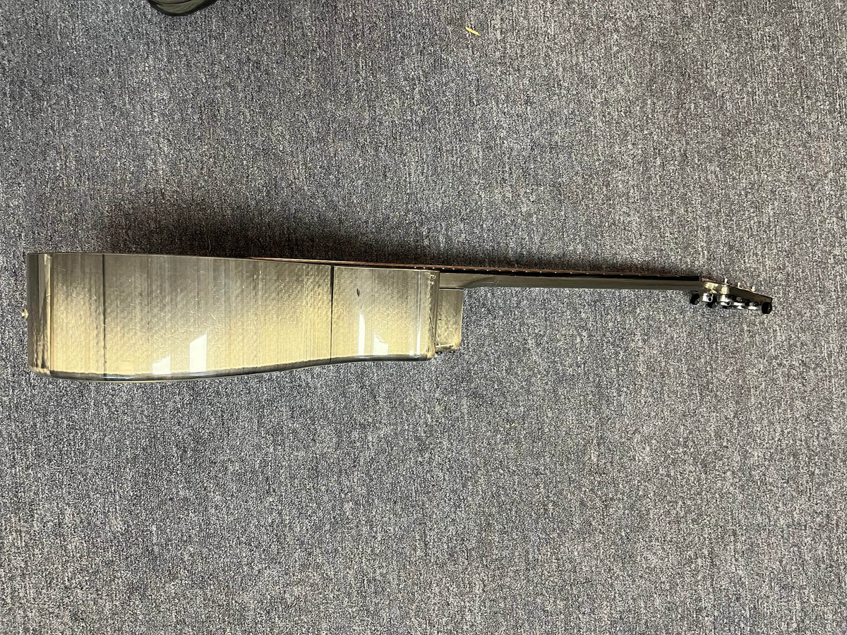 A side view of the Klos Grand Cutaway AE w/Fishman acoustic guitar lies on a gray carpeted floor, displaying its body, neck, and tuning pegs.