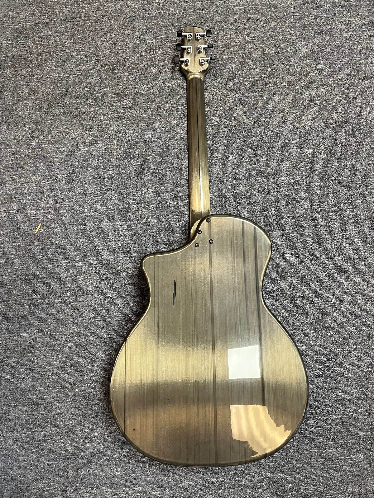 A Klos Grand Cutaway AE w/Fishman acoustic guitar with a glossy, striped back and cutaway body design lies face down on a gray carpeted floor.