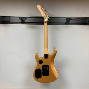 A Kramer 84 HH Killswitch electric guitar in Smoked Almond Metallic hangs on the wall, shown from the back with three black panels on the body and a wooden neck with six tuning pegs extending upward.
