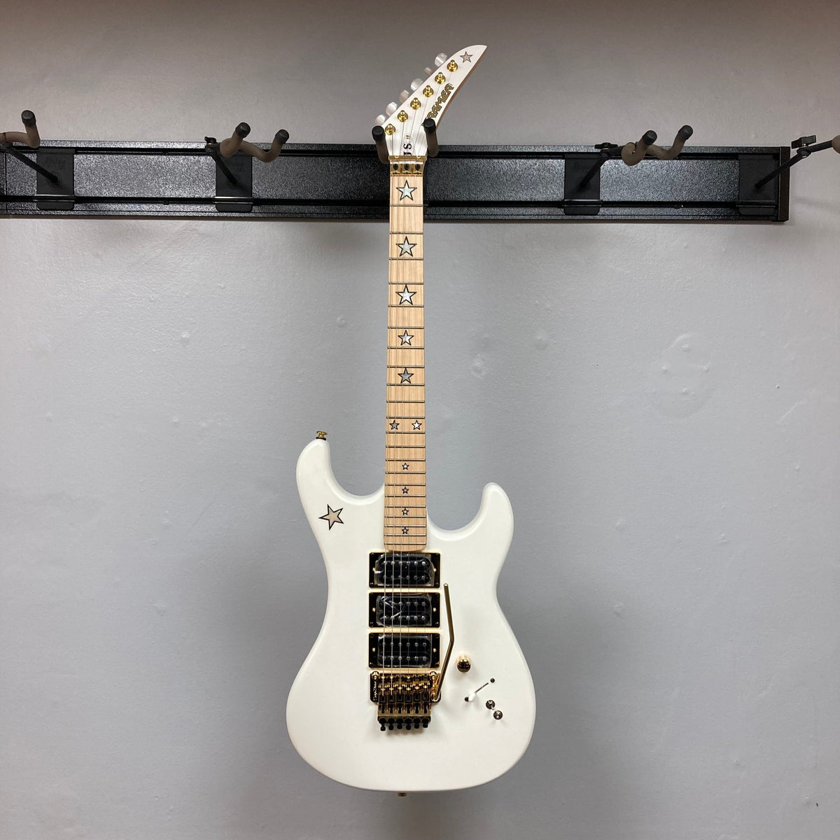 Kramer Jersey Star Pearl White electric guitar with gold hardware, star inlays, three humbucker pickups, Floyd Rose tremolo, and included gig bag.
