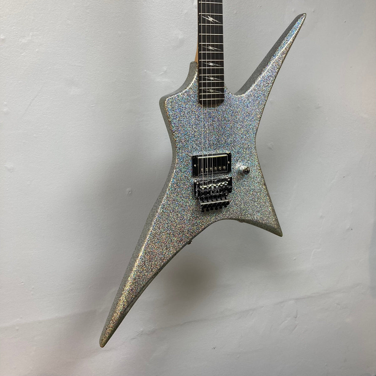 Kramer Lzzy Hale Voyager guitar with sleek design, black diamond holographic sparkle finish, and chrome hardware, hanging on a wall.