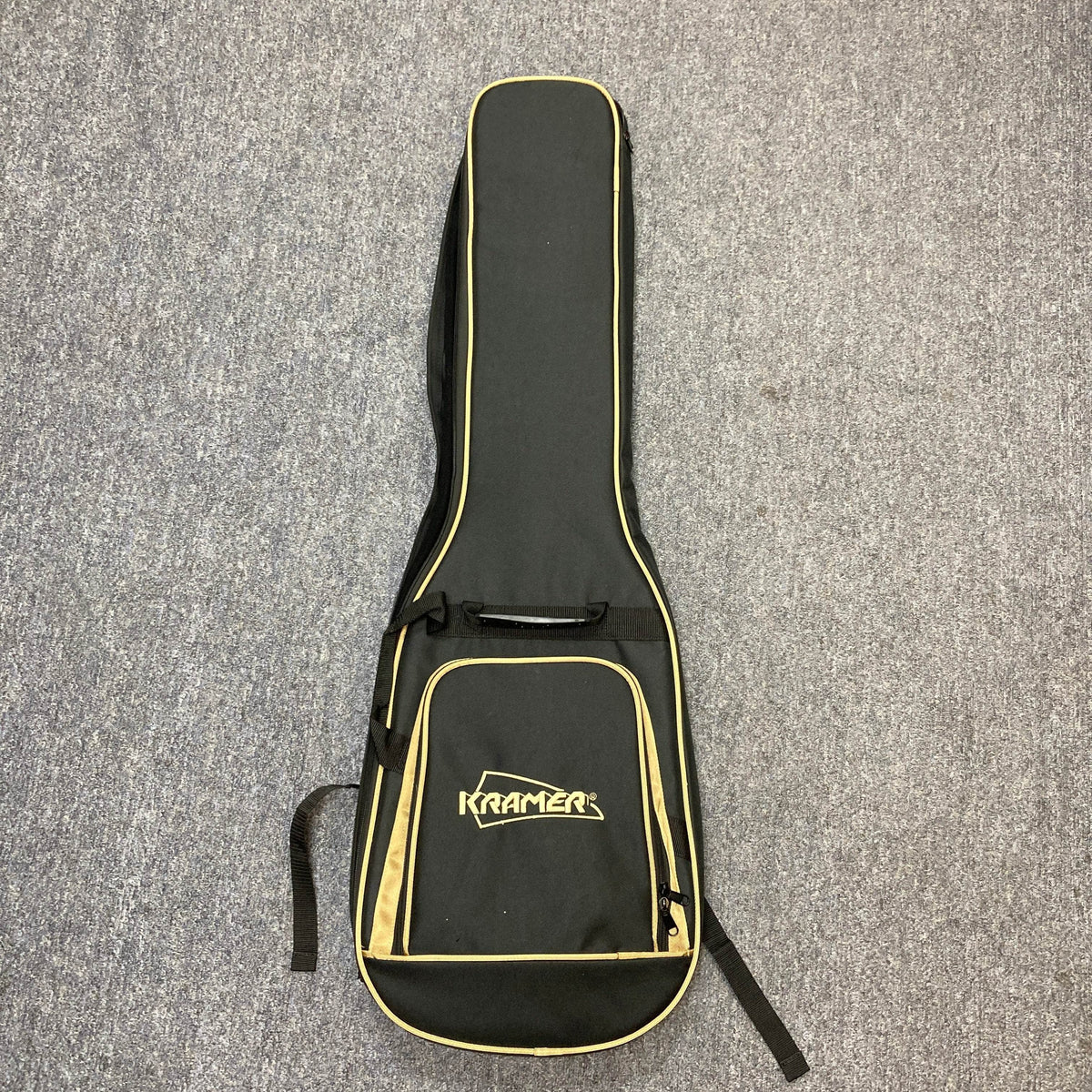 A black and yellow Kramer gigbag with the logo on the front pocket, perfect for your Kramer Volante Quilt HSFR in Aqua Burst, lies flat on a gray carpeted floor.