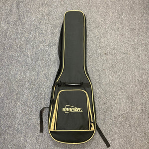 A black and yellow Kramer gigbag with the logo on the front pocket, perfect for your Kramer Volante Quilt HSFR in Aqua Burst, lies flat on a gray carpeted floor.