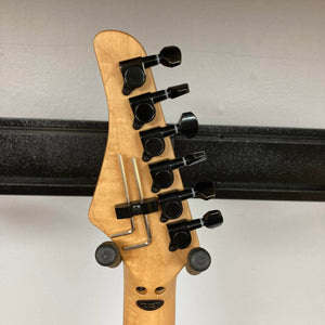 The back of a Kramer Volante Quilt HSFR, Aqua Burst by Kramer shows six black tuning pegs, a locking nut, and a metal bar on the headstock, displayed on a stand against a light gray wall. Comes with a gigbag.