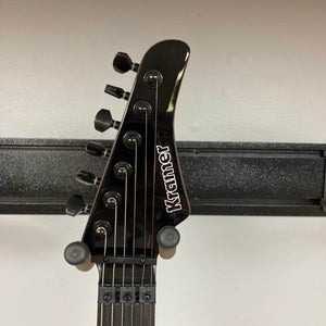 Close-up of a black Kramer Volante Quilt HSFR headstock with six tuning pegs, Floyd Rose locking nut, and white Kramer logo, set against a light wall with a black horizontal rack in the background. Brand: Kramer. Color: Aqua Burst. Includes gigbag.