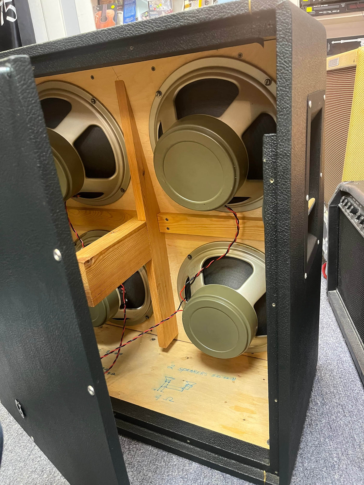 The 1969 Marshall 4x12 Cabinet with Matching Celestion T1281 Greenbacks features four vintage speakers on a wooden frame, visible wiring, and classic black exterior for authentic vintage style.
