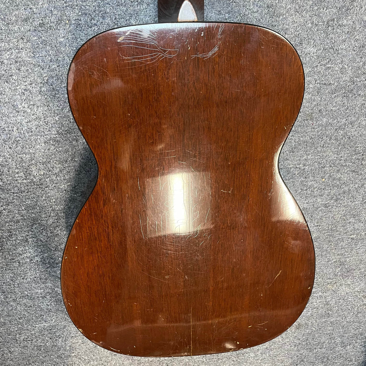 Back of a Martin 00-18G Classical Guitar (c. 1961–1962) with glossy wood finish, showing visible scratches and scuffs, set on a gray textured surface.