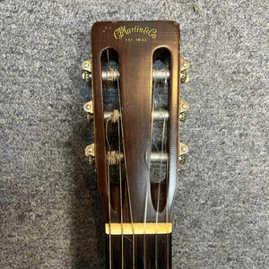 Close-up of the headstock of a Martin 00-18G Classical Guitar, c. 1961–1962 by Martin, featuring six tuning pegs and nylon strings set against a textured gray background.