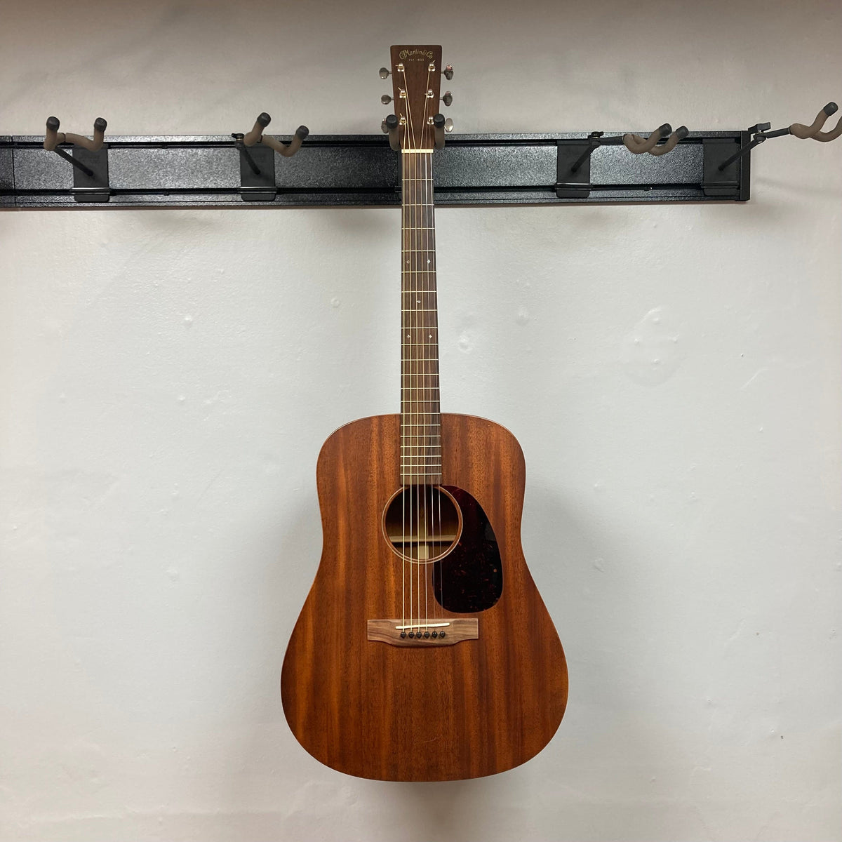 Martin D-15M acoustic guitar hanging on a wall hook, showcasing its solid mahogany construction and classic dreadnought shape.