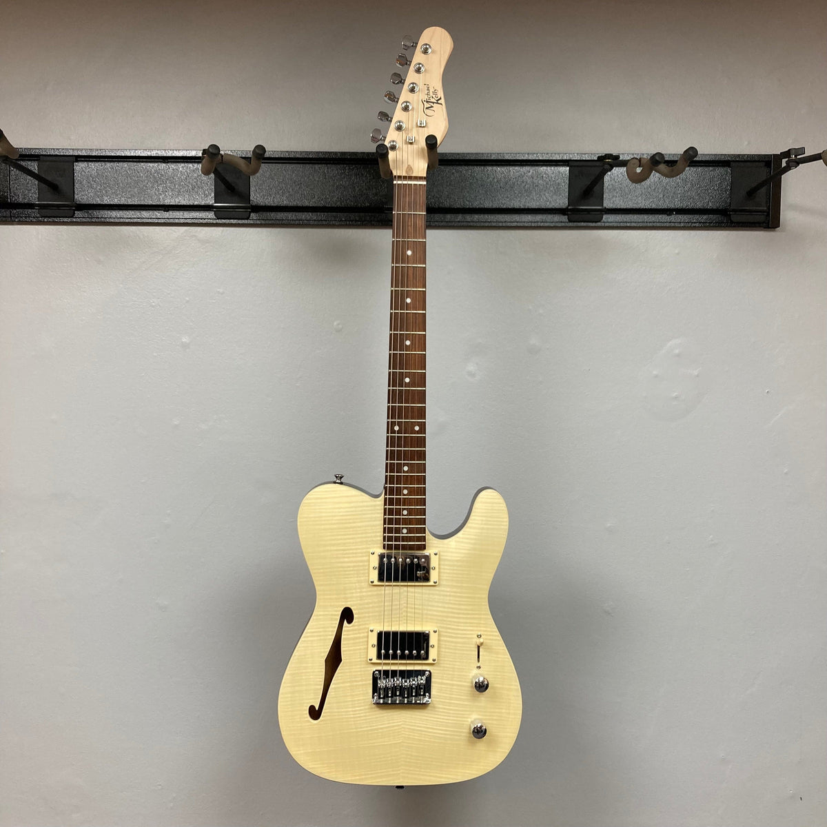 Michael Kelly 58 Tele Thinline Flame Maple Prototype Demo guitar mounted on a wall, showcasing its semi-hollow body and sleek design.