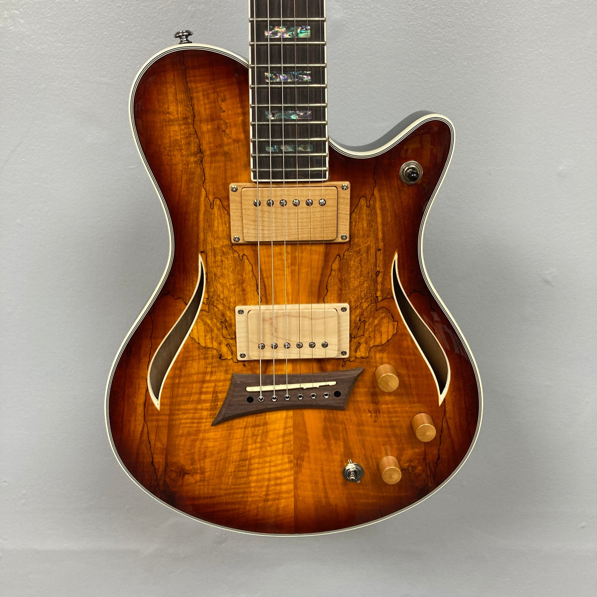 A Michael Kelly Hybrid Special Electric Guitar - Spalt Burst, featuring a glossy brown finish, semi-hollow body with two f-holes, dual pickups, three knobs, and a switch, is shown against a plain gray background.