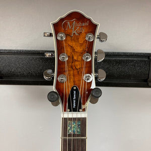Close-up of a Michael Kelly Hybrid Special Electric Guitar - Spalt Burst headstock, showing six tuning pegs, dark wood finish, and the Michael Kelly logo. The guitar is displayed on a wall hanger against a plain background.