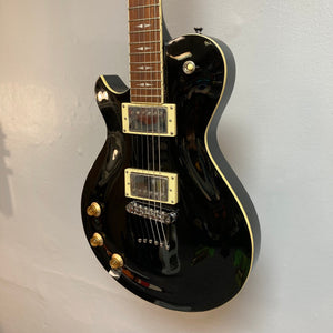 Black electric guitar with gold hardware, Patriot Decree Lefty Black Blem model, featuring PAF pickups, mahogany body and neck, chrome hardware, and a Tune-O-Matic bridge.