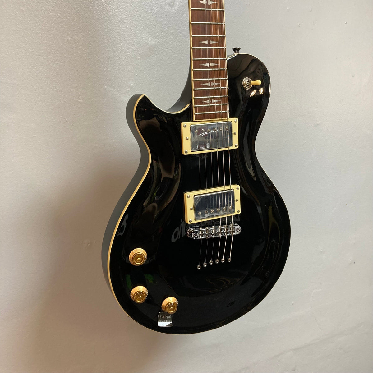 Michael Kelly Patriot Decree Lefty Black Blem, a black electric guitar with mahogany body and PAF pickups, mounted on a wall.