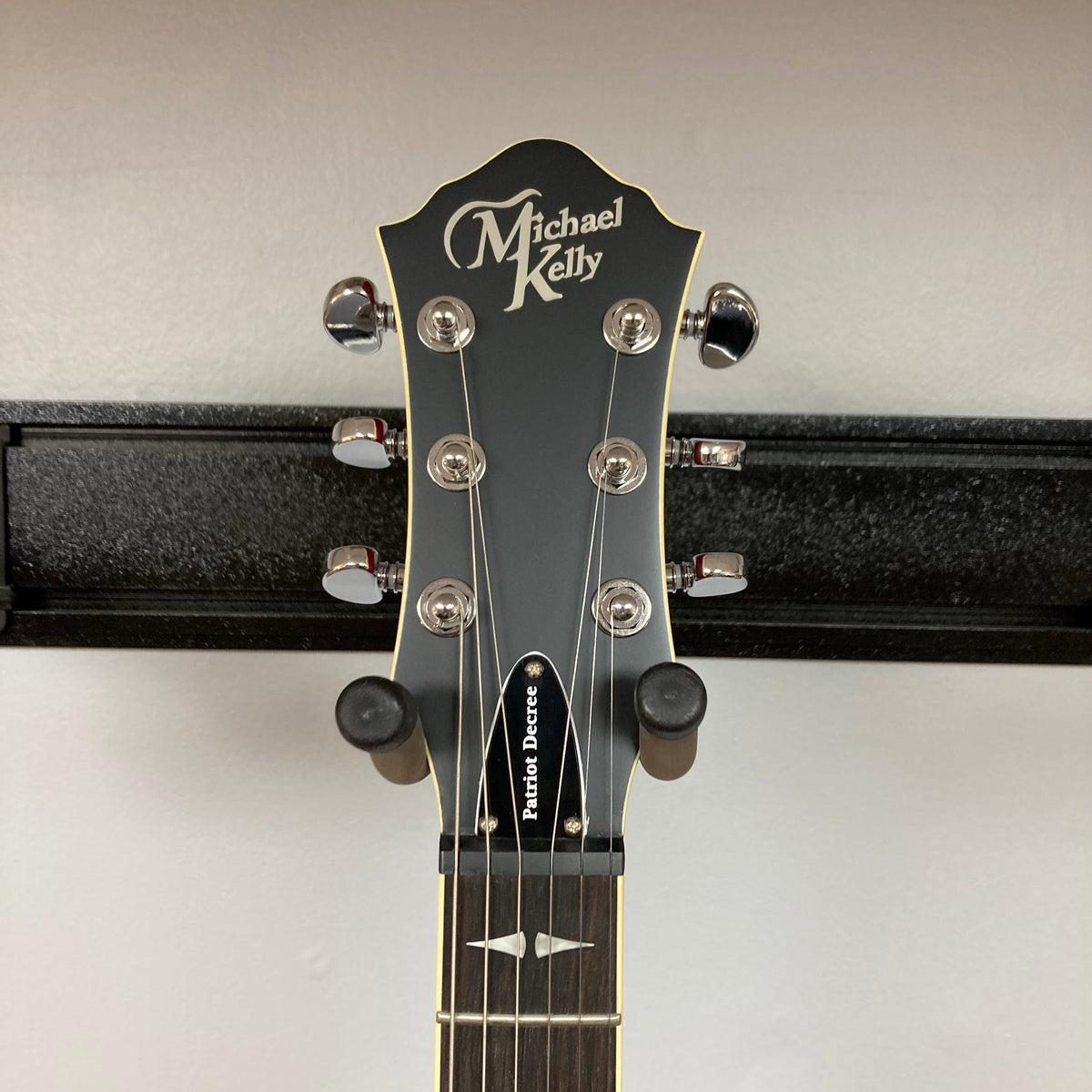 Michael Kelly Patriot Decree Open Pore Slim Body Cherry Red guitar on a stand, featuring a sleek design and Rockfield humbucker pickups.