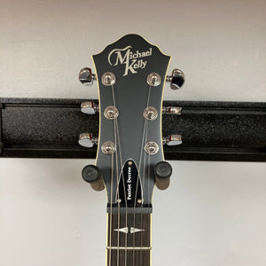 Michael Kelly Patriot Decree Open Pore Slim Body Cherry Red guitar on a stand, featuring a sleek design and Rockfield humbucker pickups.