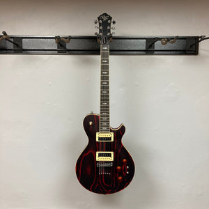 Michael Kelly Patriot Decree Open Pore Slim Body Cherry Red guitar mounted on a wall, showcasing its sleek design and dual humbucker pickups.
