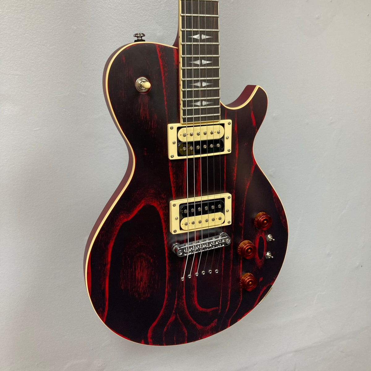 Michael Kelly Patriot Decree Open Pore Slim Body Cherry Red guitar with dual humbucker pickups, toggle switches, and ebony fretboard displayed on a wall.