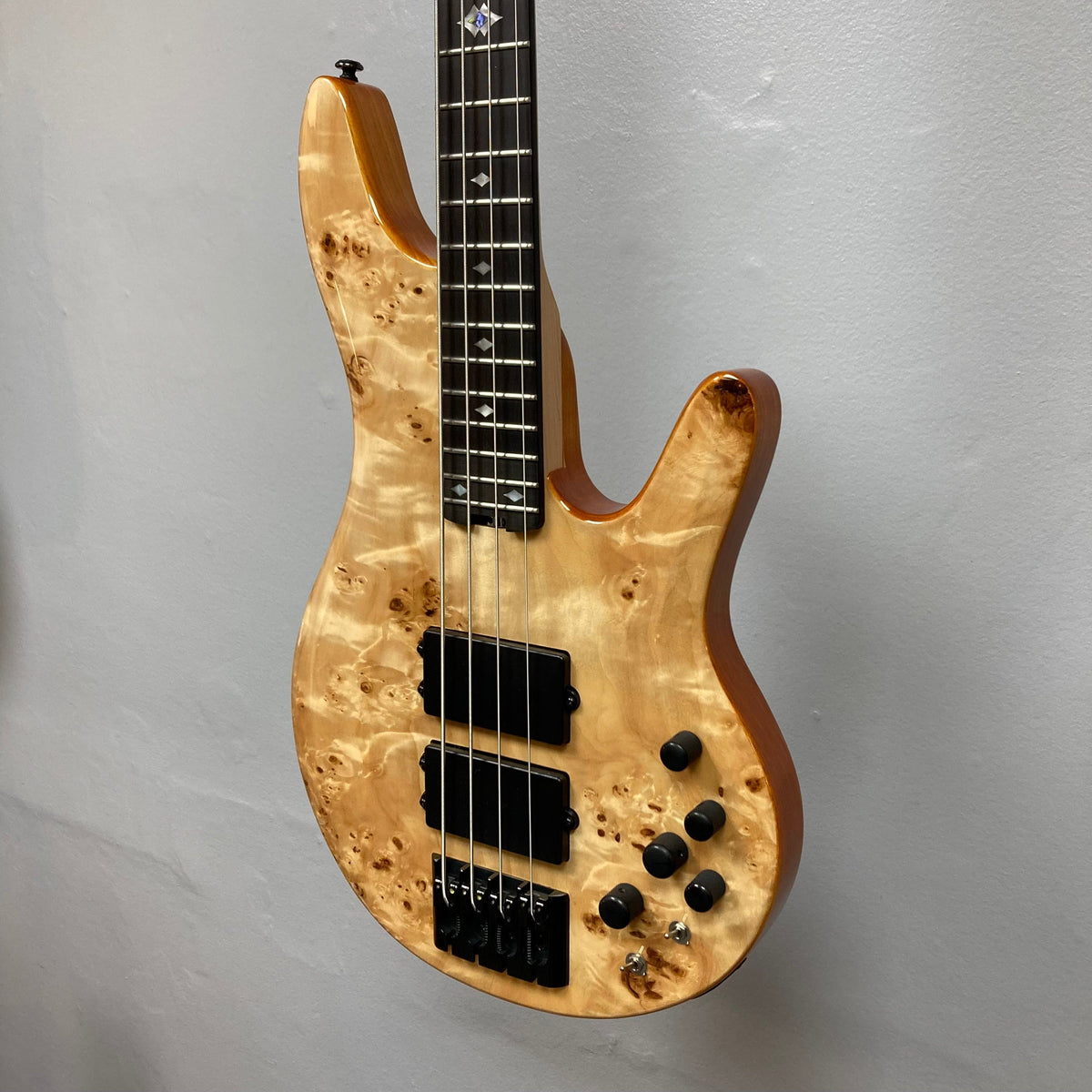 Close-up of the Michael Kelly Pinnacle 4 Bass guitar, showcasing its intricate burl poplar top, diamond inlays, and Rockfield MDC4 humbucker pickups.