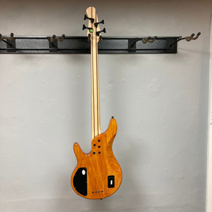 Michael Kelly Pinnacle 4 Bass on a hook, highlighting its swamp ash body, burl poplar top, and five-piece maple and walnut neck.