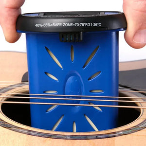 A person inserts the Music Nomad The Humitar ONE – Acoustic Guitar Humidifier & Hygrometer by Music Nomad into an acoustic guitar’s soundhole, using its labeled safe humidity and temperature ranges to monitor and protect the instrument.