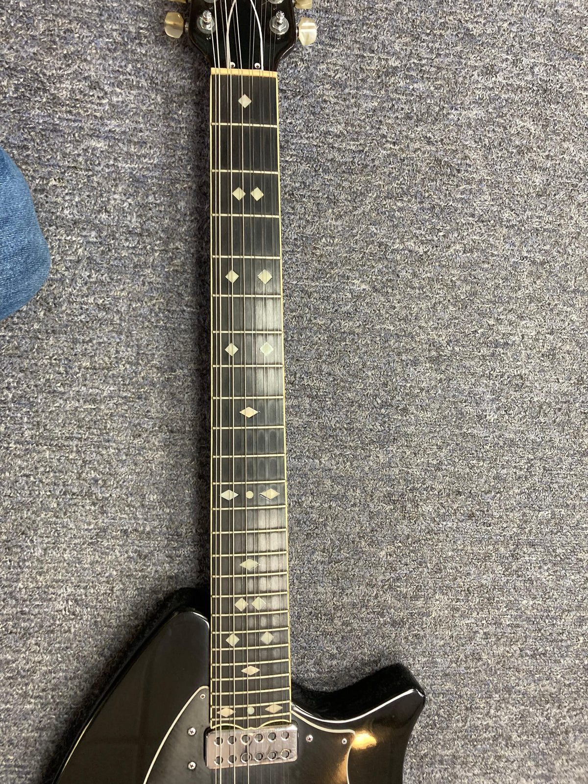 Ovation Deacon 12-String Electric Guitar in black on a carpet, showcasing its strings and body.