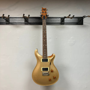 PRS 1996 Gold Top electric guitar with black neck, mounted on a wall, showcasing its vintage charm and craftsmanship.
