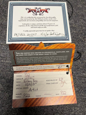 Certificate of authenticity and quality control card for the PRS P22 Artisan Piezo Green Fade 2013 Brazilian Rosewood w/Case, showing model, serial number, neck type, date, and inspection details on a gray surface.