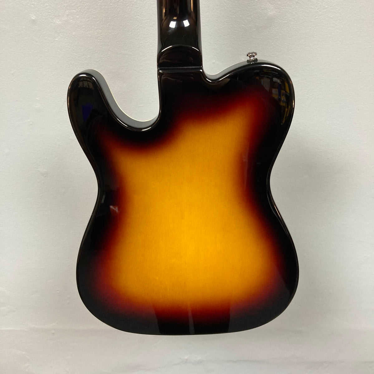 The back of the Reverend Greg Koch Signature Gristle 90 electric guitar in 3-Tone Burst, with dark edges fading to a bright yellow center, is photographed against a plain white wall.