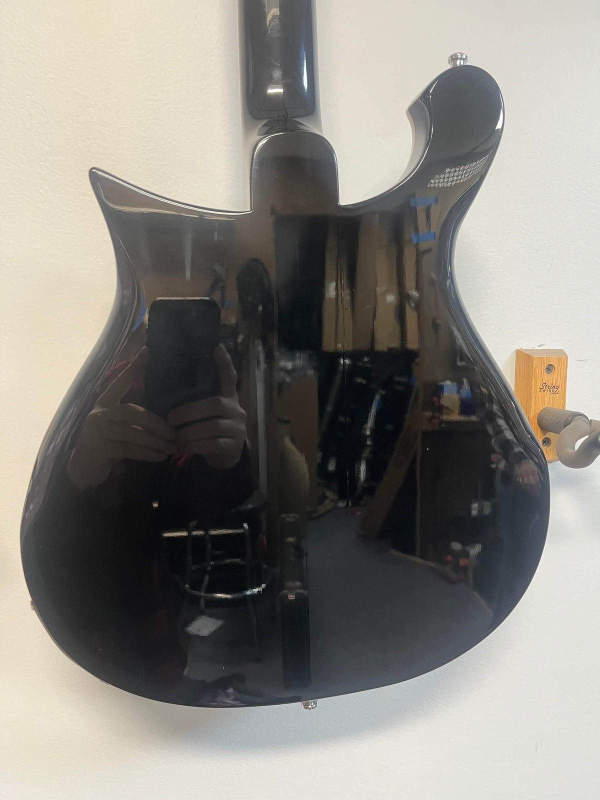 The back of a near-mint Rickenbacker 620 – Jetglo hangs on a wall, its glossy finish reflecting the photographer and room; includes original case.