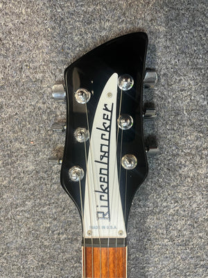A close-up of a near-mint Rickenbacker 620 Jetglo headstock with tuning pegs and logo, photographed on a grey textured surface. Includes original case.