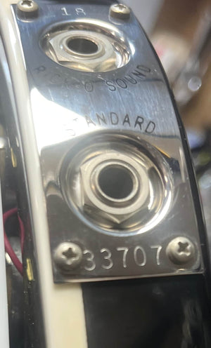 Close-up of a hand holding the side of a near-mint Rickenbacker 620 electric guitar in Jetglo finish, featuring input jacks, control knobs, and serial number 33707. Workshop tools appear in the background. Original case included.