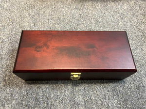 A closed rectangular wooden box with a reddish finish and gold-colored latch, often used for the Royer Labs R-121 Ribbon Microphone (Pre-owned in excellent condition), rests on a gray carpeted surface.