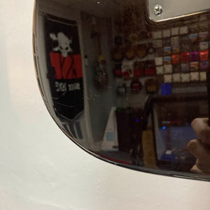 A room with shelves, a skull flag, and a person holding a Schecter Extreme Banshee 6 FR CHARCOAL BURST electric guitar is reflected on its glossy surface.