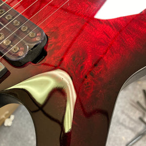 Schecter Omen Elite-7 Left-handed Black Cherry Burst Blemish, close-up view of red guitar body and strings, highlighting intricate burl top and Heretic pickups.