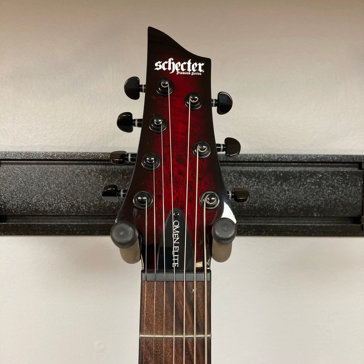 Schecter Omen Elite-7 Left-handed Black Cherry Burst Blemish on stand, showcasing its burl top and Heretic pickups.