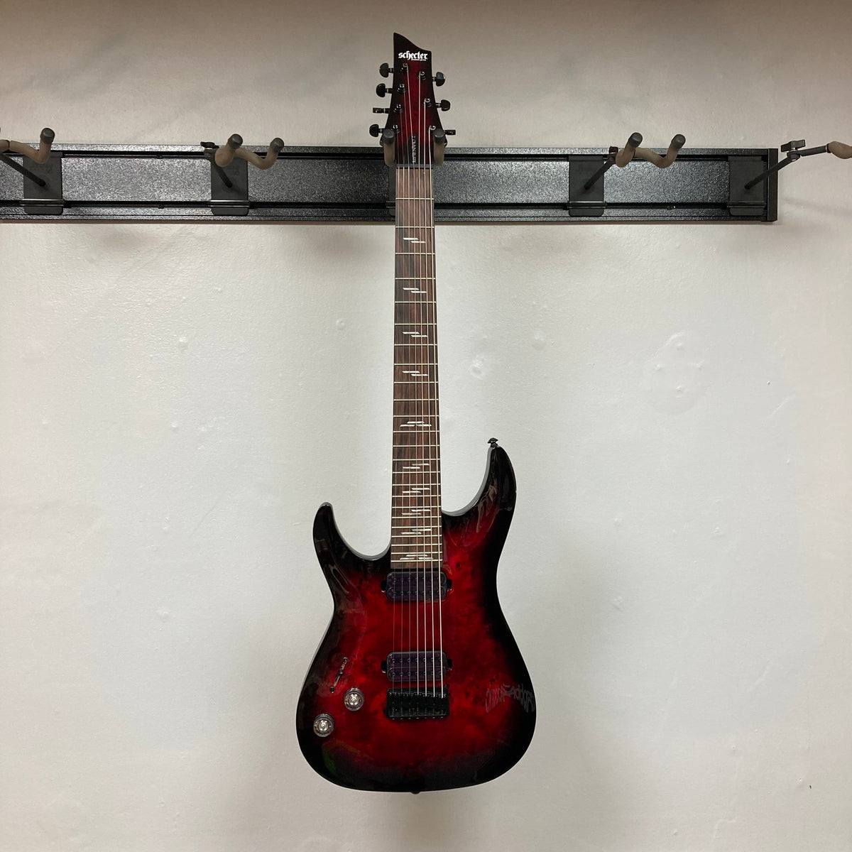 Schecter Omen Elite-7 Left-handed Black Cherry Burst Blemish, a seven-string red electric guitar displayed on a wall, featuring Heretic pickups and mahogany-maple construction.