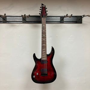 Schecter Omen Elite-7 Left-handed Black Cherry Burst Blemish, a seven-string red electric guitar displayed on a wall, featuring Heretic pickups and mahogany-maple construction.