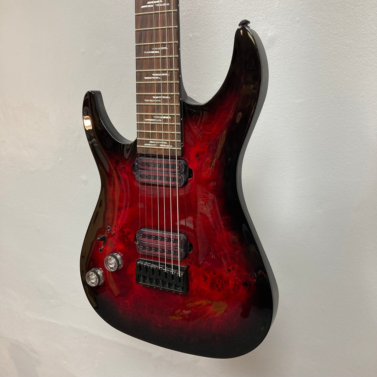 Schecter Omen Elite-7 Left-handed Black Cherry Burst Blemish, featuring a burl top, seven strings, and Heretic pickups, showcased in a close-up of the guitar's body and strings.