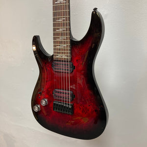 Schecter Omen Elite-7 Left-handed Black Cherry Burst Blemish, featuring a burl top, seven strings, and Heretic pickups, showcased in a close-up of the guitar's body and strings.